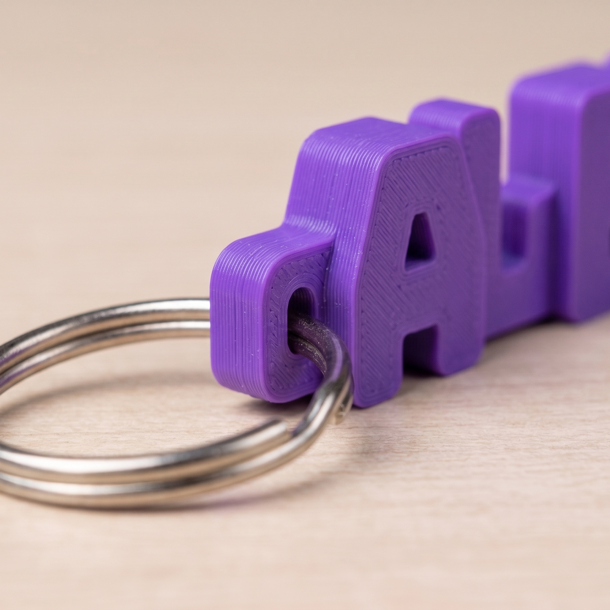 Close-up of a purple 3D printed name keychain with a metal key ring