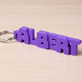 Purple custom 3D printed name keychain reading ALBERT on a wooden table