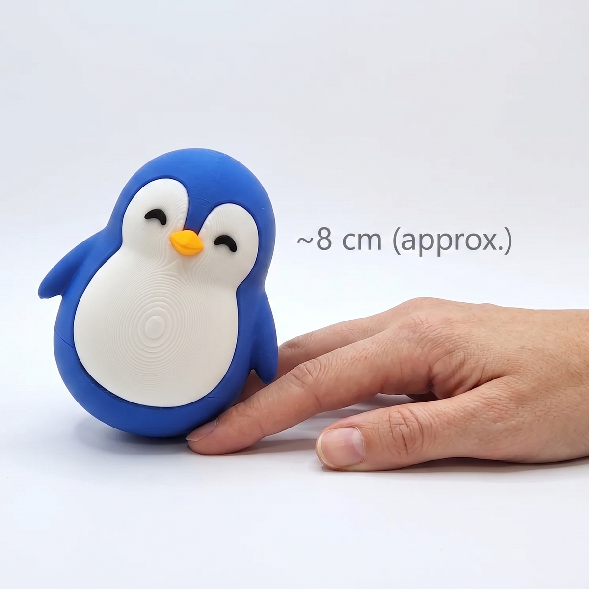 Chubby penguin figurine next to a hand showing its approx. 8 cm size