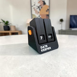 Black Date Keeper perpetual flip calendar on a white table in a living room