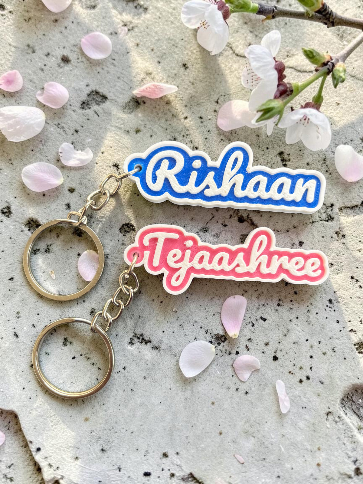 Rishaan and Tejaashree 2-colour name keychains on stone with flower petals