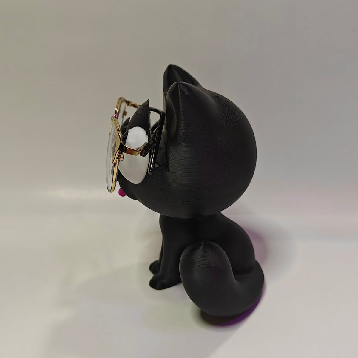 Swag Layers black 3D printed cat glasses holder with gold-rimmed spectacles on a white background