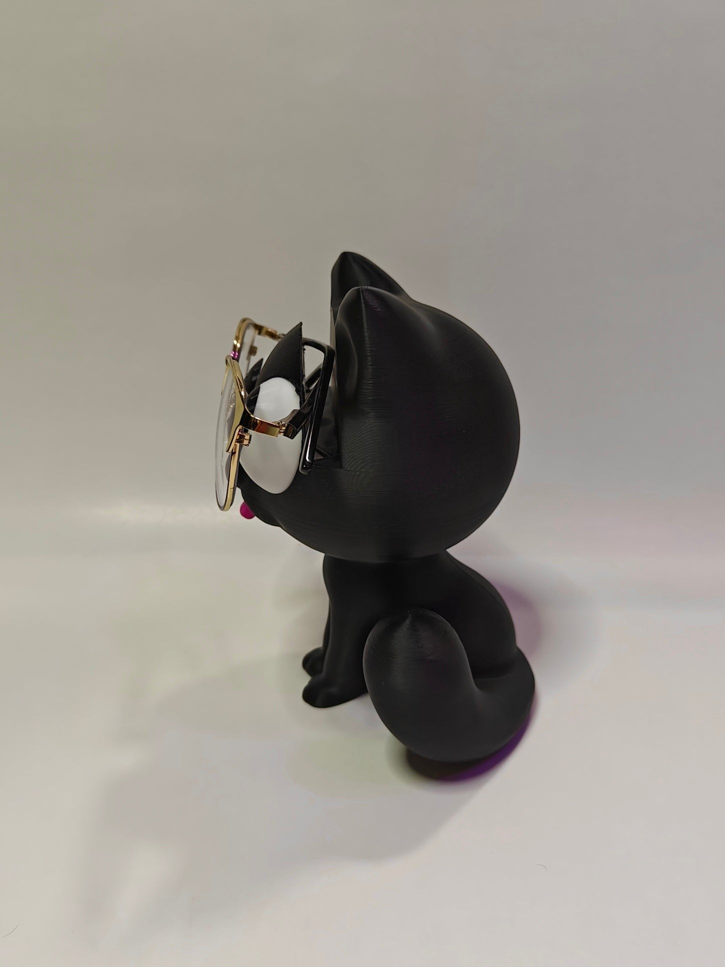 Swag Layers black 3D printed cat glasses holder with gold-rimmed spectacles on a white background