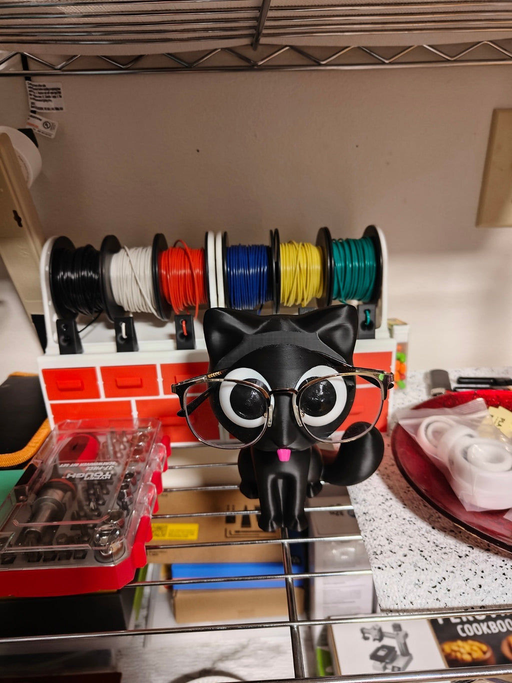 Swag Layers PurrRest black 3D printed cat glasses holder with large eyes wearing gold-rimmed spectacles on a desk