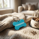 Swag Layers custom blue 3D-printed bone-shaped dog tag with phone number, resting on a cozy knit blanket.